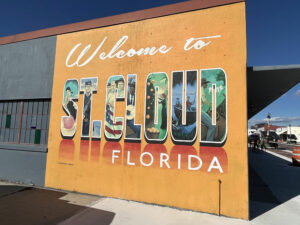 Famous "Welcome to St. Cloud Florida" mural located on Pennesalvania Ave in downtown St. Cloud. The mural background is bright orange and the text "St Cloud" is in block letters. Different images are painted within the block lettering.
