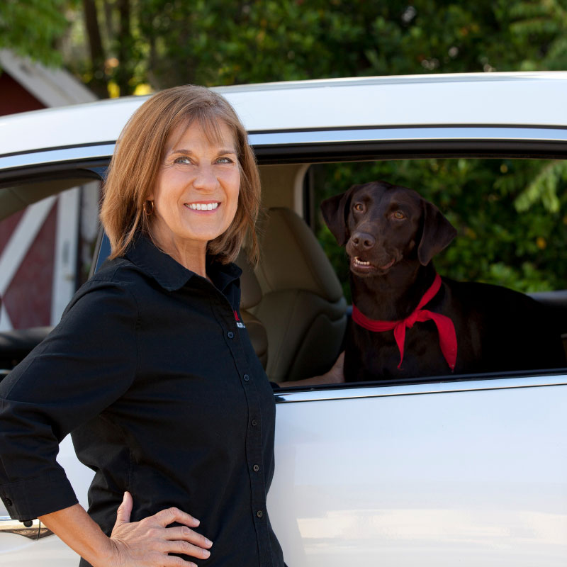 Dawn Grigsby, St Cloud Florida Real Estate Agent, posing with her black lab dog inside of a white car.